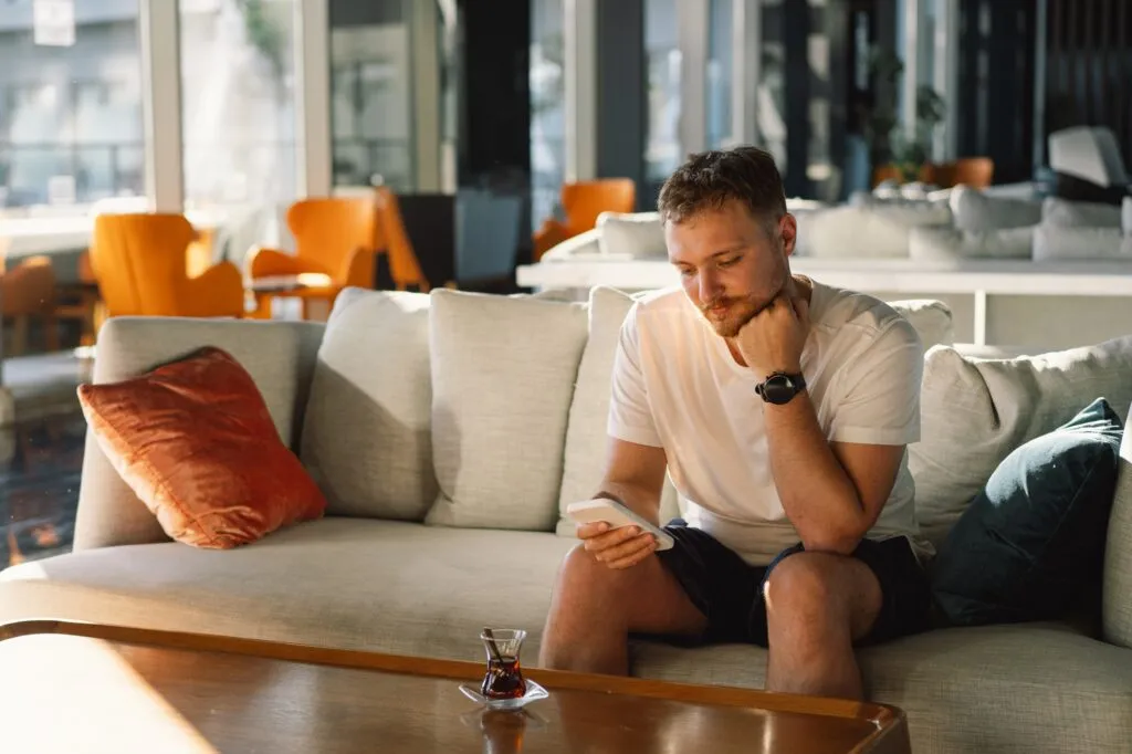 Young happy man using mobile phone in hotel lobby.